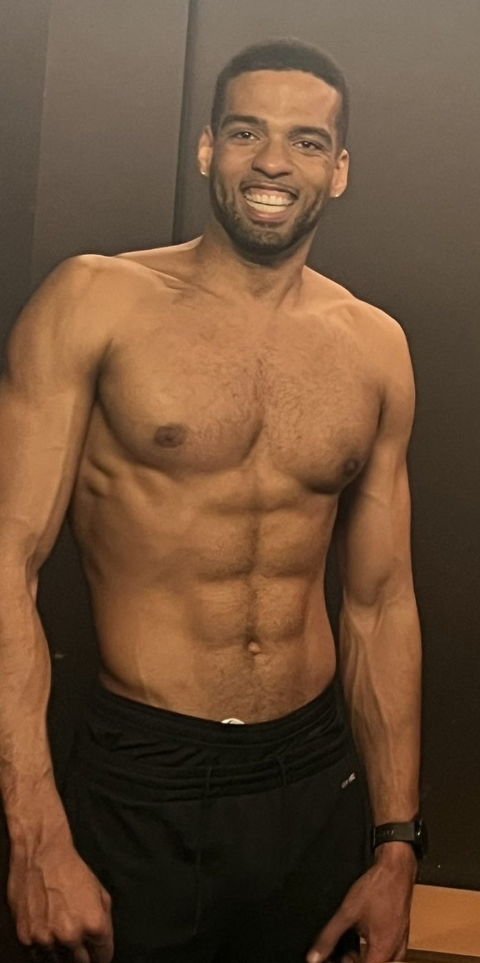 Manu hoy, sonriendo, con el torso definido sobre fondo oscuro