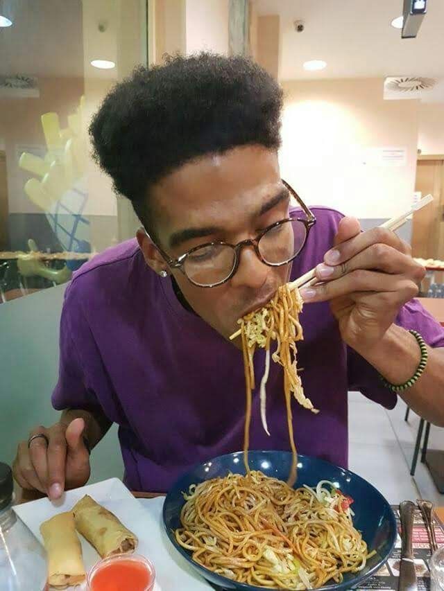 Manu, muy delgado, comiendo un plato enorme de fideos con palillos